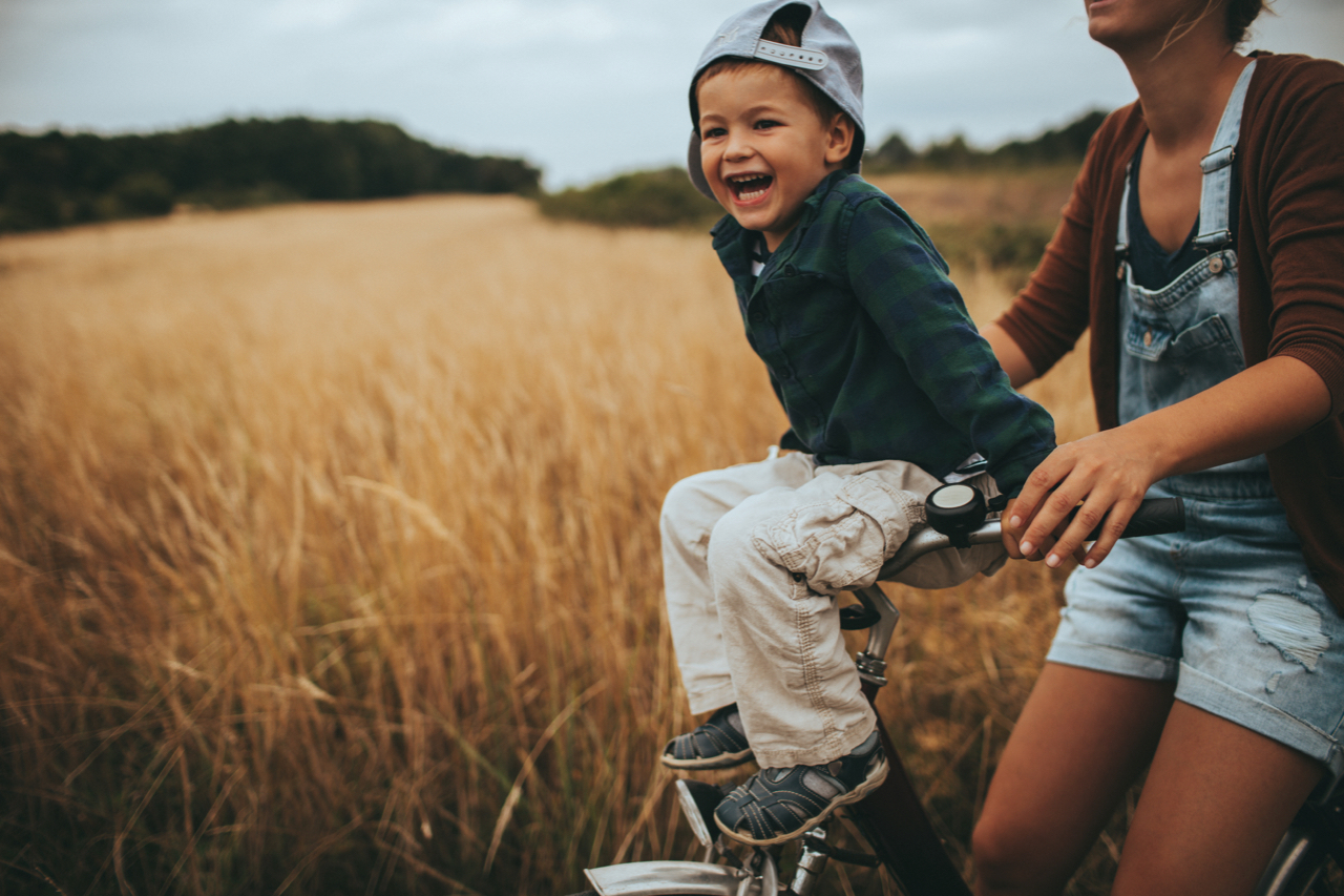 Little boy and his mother are riding a bicycle outdoors in the nature. Boy is sitting on a wheel